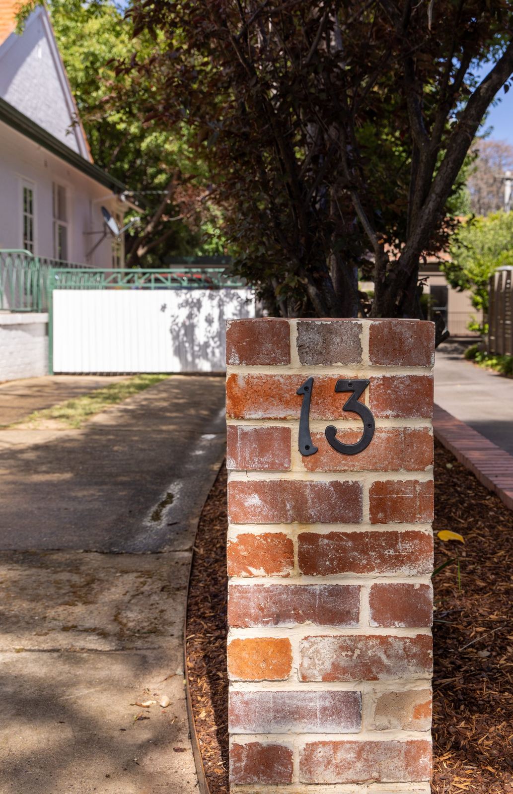 Brick entry pillar with the house number, brick-edged garden bed and an established tree