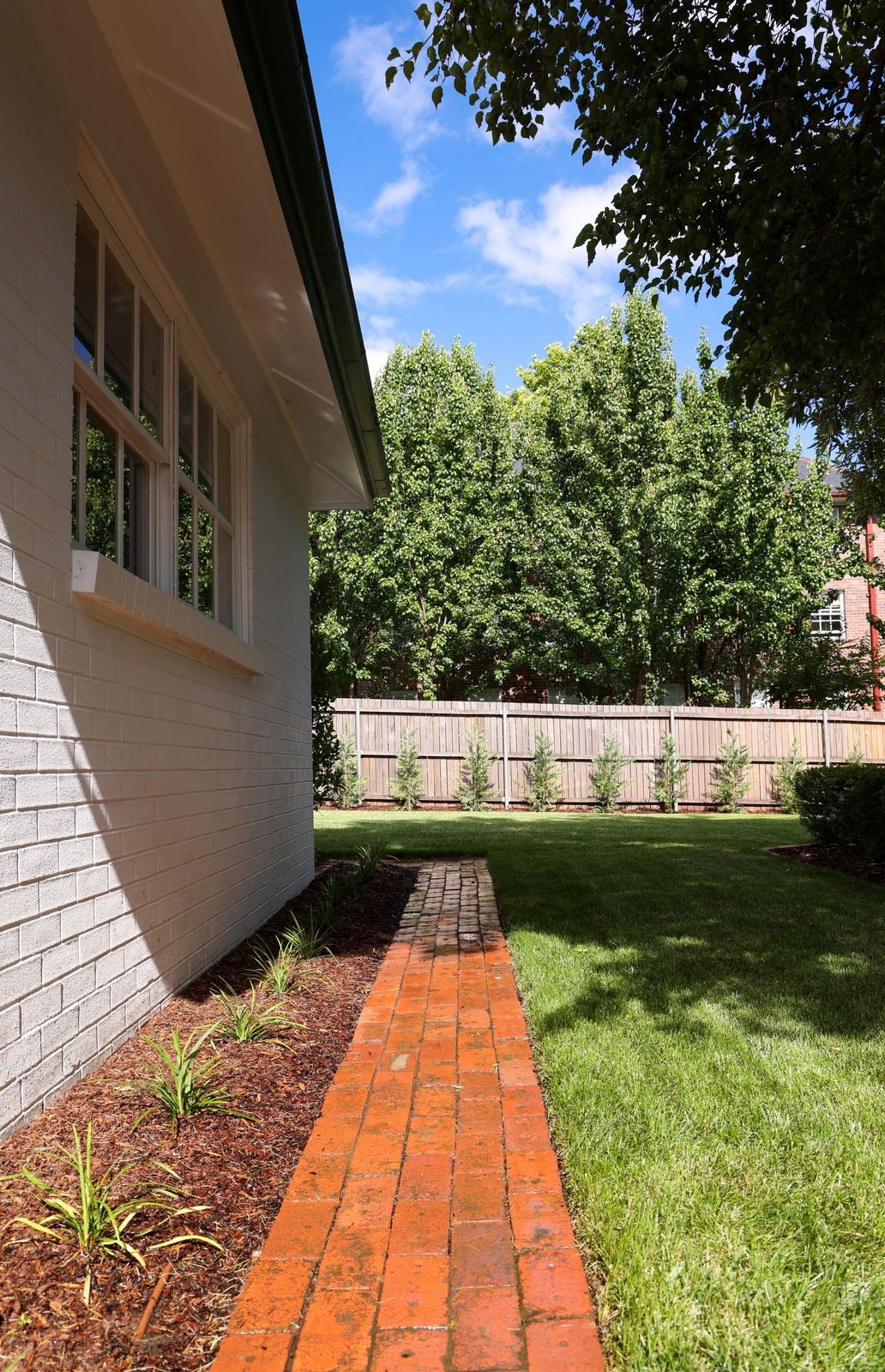 Side of the cottage with a new brick-edged garden bed and fresh planting