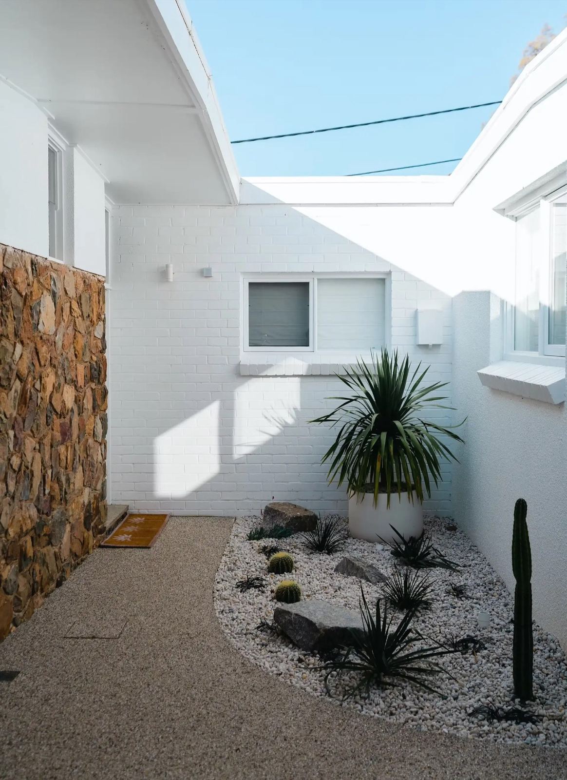 Dugan Street Deakin: white-brick courtyard with stone feature wall and desert planting