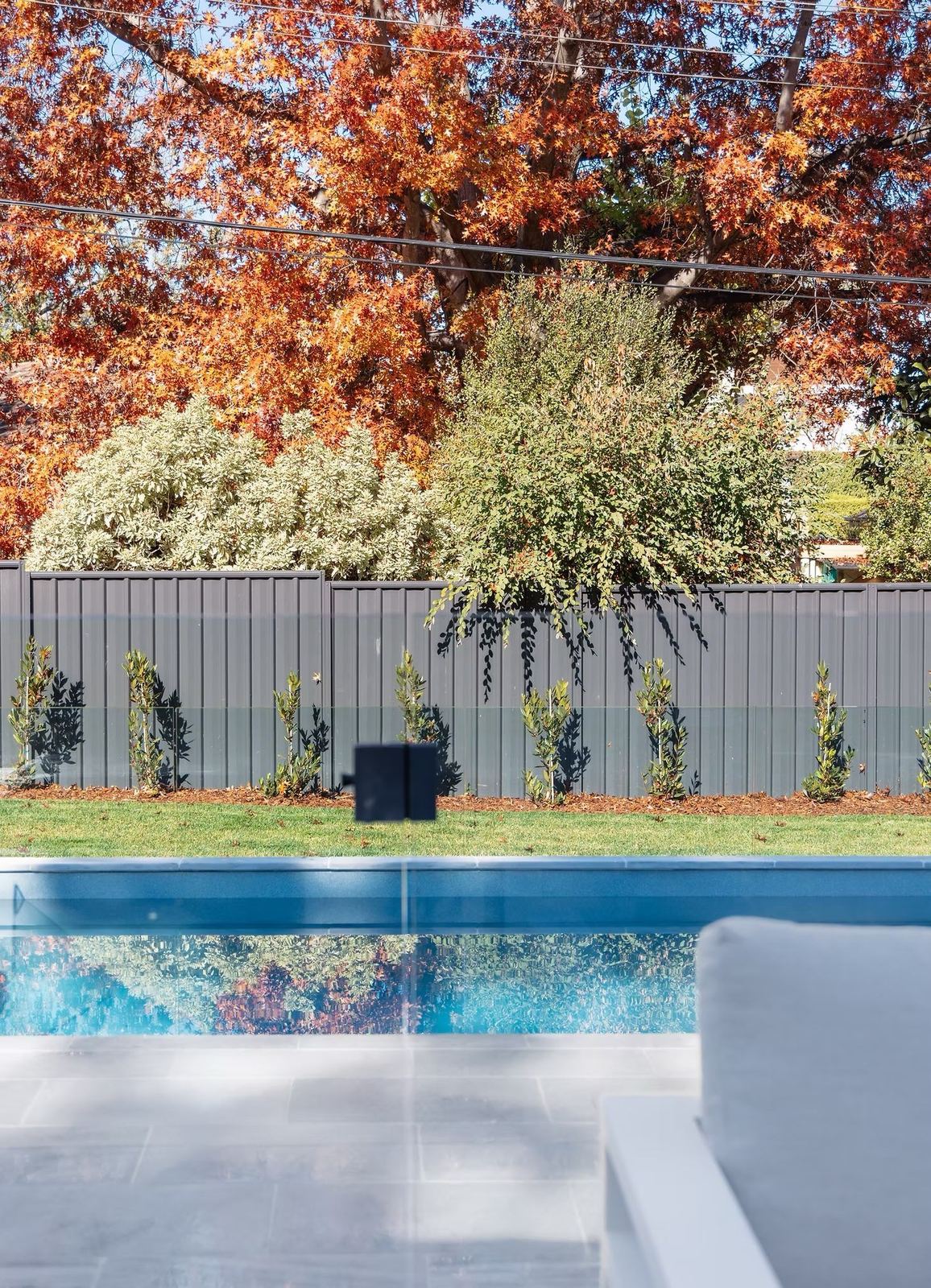 Pool and spa step edged in stone paving, with an autumn tree and dark boundary fence behind