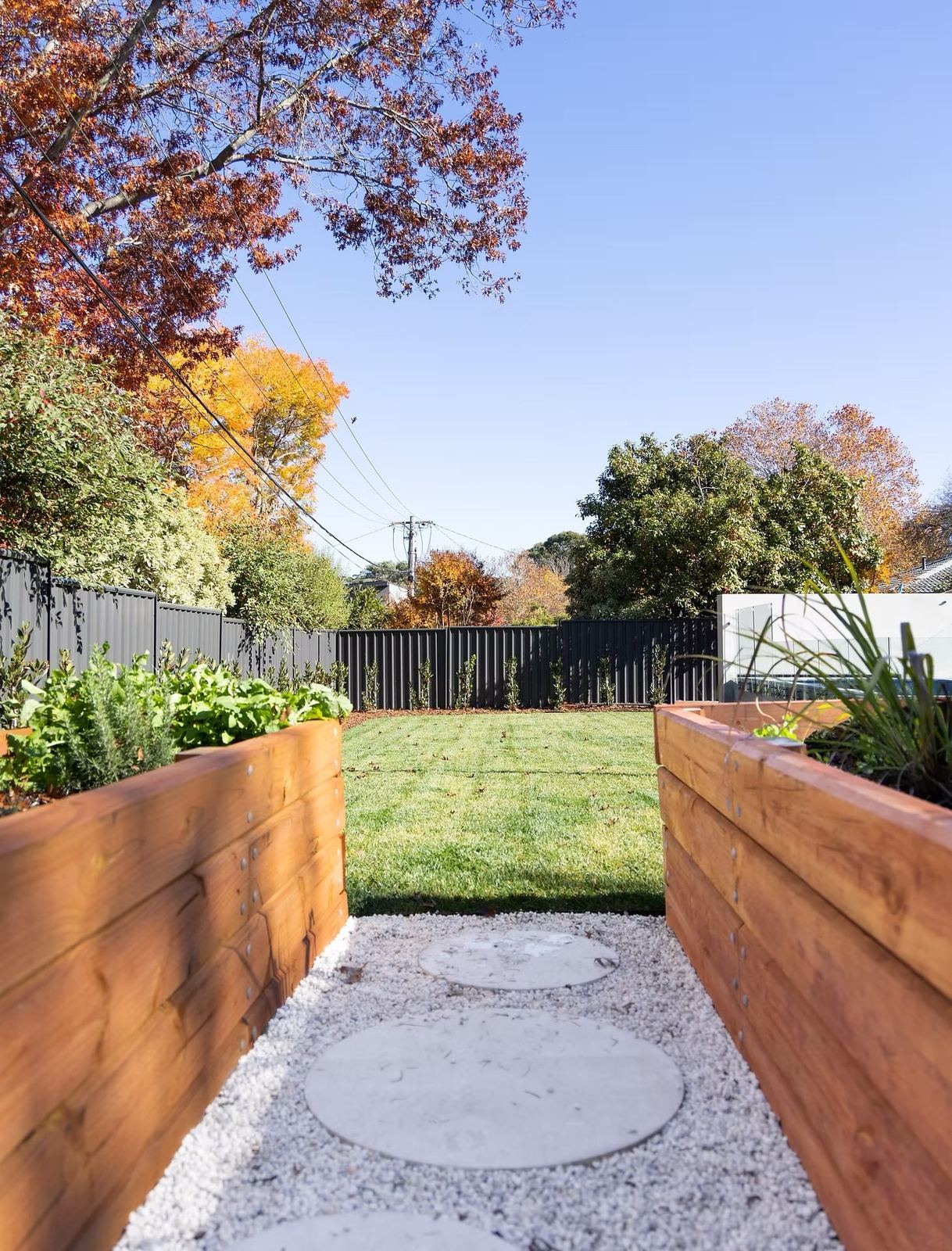 Raised timber garden beds along a gravel path with a circular stepping pad and lawn